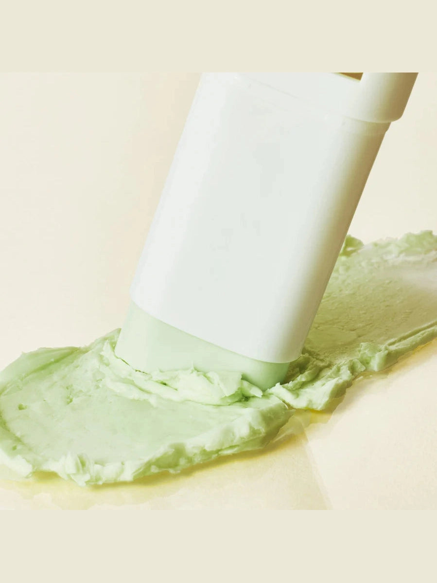 White spatula spreading green cream on a beige background